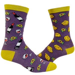 May include: A pair of purple socks with a yellow cuff. The socks feature a repeating pattern of wine bottles, wine glasses, and cheese wedges.