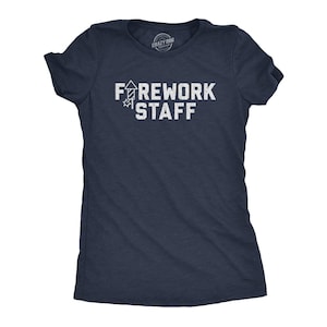 May include: A navy blue short-sleeve t-shirt with a white graphic print on the chest. The text reads FIREWORK STAFF, with the letter I replaced by a rocket icon. The design has a distressed, weathered texture and a crew neckline.