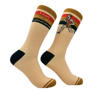 Könnte beinhalten: Ein Paar beigefarbene Socken mit schwarzen und braunen Streifen. Die Socken zeigen eine laufende Figur und den Text "Ich laufe besser als die Regierung".