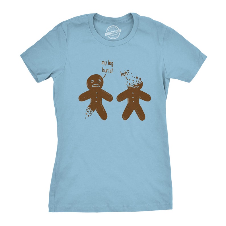 May include: Light blue t-shirt with a humorous graphic of two gingerbread men. One has a broken leg and says "my leg hurts!" The other has a cracked head and says "huh?". The shirt has the "Crazy Dog" logo at the top.