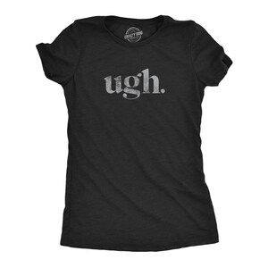 May include: A black short-sleeved t-shirt featuring the word ugh. printed in a distressed white font across the chest. The garment has a crew neckline and a small circular brand logo printed on the inside of the collar area.