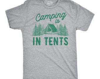 May include: A heather gray short-sleeve t-shirt featuring a green graphic of a tent surrounded by pine trees. The text "Camping is IN TENTS" is printed in green above and below the tent illustration in a mix of script and block lettering.