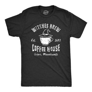 Può includere: Una t-shirt grigio antracite a maniche corte con una grafica bianca raffigurante una tazza di caffè sormontata da un cappello da strega. Il testo recita Witches Brew, Est. 1692, Coffee House e Salem, Massachusetts in stile usurato.