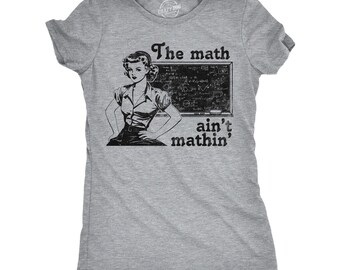 Könnte beinhalten: Ein graumeliertes Kurzarm-T-Shirt mit einem schwarzen Grafikdruck einer Person vor einer mit Gleichungen beschriebenen Tafel. Der Text "The math ain't mathin'" ist in einer fetten, dunklen Schrift über und unter der Tafel aufgedruckt.