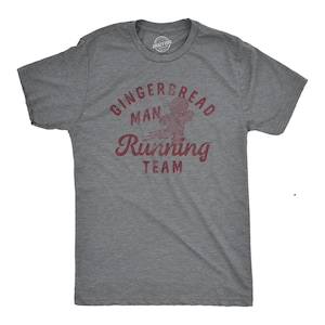 May include: A heather gray t-shirt with the words "Gingerbread Man Running Team" in burgundy. The graphic features a gingerbread man in motion. The shirt has a crew neck and short sleeves.