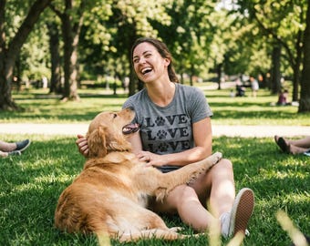 May include: A heather gray short-sleeve t-shirt featuring the word LOVE printed three times in black, with a black paw print replacing the letter O in each instance. The shirt has a crew neckline and is made of a soft, casual fabric material.