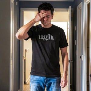 May include: A black short-sleeved t-shirt featuring the word "ugh." printed in a light gray, distressed serif font across the chest. The garment is paired with blue denim jeans, creating a casual look with a simple, bold graphic design.
