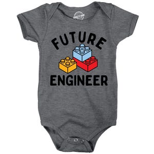 May include: A dark heather grey short-sleeve baby bodysuit featuring the text FUTURE ENGINEER in black capital letters. Between the words are three stacked plastic building blocks in light blue, red, and yellow with circular studs on top.