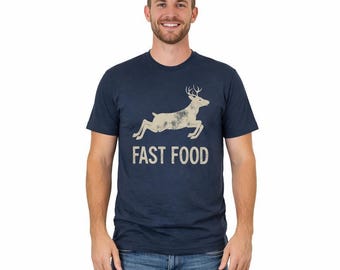 May include: A navy blue short-sleeve t-shirt featuring a distressed beige graphic of a leaping deer above the text "FAST FOOD" in a bold, sans-serif font. The shirt has a crew neckline and a standard fit, constructed from a soft fabric.