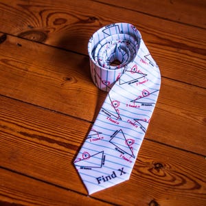 May include: A white necktie featuring a blue-lined notebook paper pattern with black geometric triangle diagrams, red circled X marks, and the repeated red text "I found it." The bottom of the tie displays the black text "Find X."
