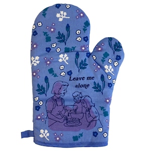 May include: Blue oven mitt with a floral pattern and the text "Leave me alone". The mitt features a cartoon image of three people baking a cake.