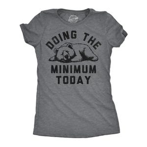May include: A heather gray short-sleeve t-shirt featuring a black graphic of a sleeping bear. Above the bear, the text reads DOING THE, and below the bear, the text reads MINIMUM TODAY. The shirt has a crew neckline and a standard fit.