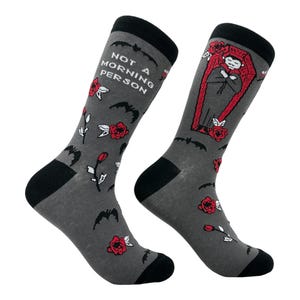 Könnte beinhalten: Ein Paar graue Socken mit schwarzem Bündchen. Eine Socke hat ein Motiv eines Vampirs in einem Sarg mit roten Rosen und Fledermäusen. Die andere Socke hat den Text "Not a Morning Person" mit Fledermäusen und roten Rosen.