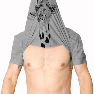 Könnte beinhalten: Ein graumeliertes Kurzarm-T-Shirt, das über den Kopf gezogen wurde und eine schwarz-weiße grafische Illustration eines Giraffengesichts mit herausgestreckter Zunge auf dem Stoff zeigt, der den Kopf und den oberen Brustbereich bedeckt.