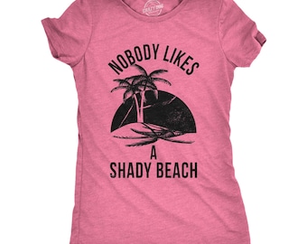 Puede incluir: Una camiseta de manga corta en color rosa jaspeado con un gráfico negro de una palmera en una pequeña isla frente a un sol oscuro. El texto NOBODY LIKES A SHADY BEACH está impreso en letras mayúsculas negras sobre y bajo la ilustración.