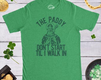 Könnte beinhalten: Ein kurzärmeliges T-Shirt in Heidekrautgrün mit einer dunkelgrünen Grafik einer bärtigen Figur, die einen Stab hält. Der Text lautet THE PADDY DON'T START TIL I WALK IN. Das T-Shirt hat einen Rundhalsausschnitt und eine Standardpassform, flach liegend.