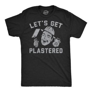 Puede incluir: Camiseta negra con la frase "LET'S GET PLASTERED". El gráfico muestra a un hombre sonriente con un casco, sosteniendo una llana y una lata. El logotipo de Crazy Dog está en la parte superior.
