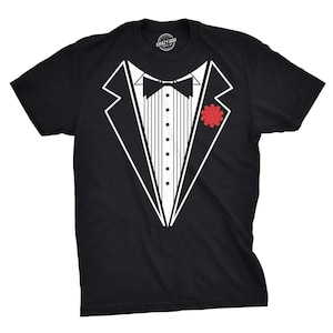 May include: A black short-sleeve t-shirt featuring a white graphic print of a tuxedo jacket, including a black bow tie, a white pleated shirt front with black buttons, and a red flower boutonniere on the left lapel. The shirt has a crew neckline.