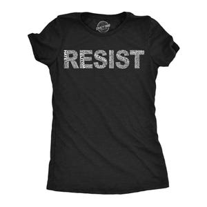 May include: A black short-sleeved t-shirt featuring the word RESIST printed in large white letters across the chest. The letters are composed of smaller white words including HATE, ELITISM, SEXISM, RACISM, INEQUALITY, and HOMOPHOBIA.