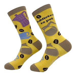 May include: A pair of yellow socks with brown heels and toes. The socks feature coffee-themed graphics, including coffee beans, a purple espresso maker, a blue cup, and a coffee pot. The text "Addicted to pot" is printed on one sock.
