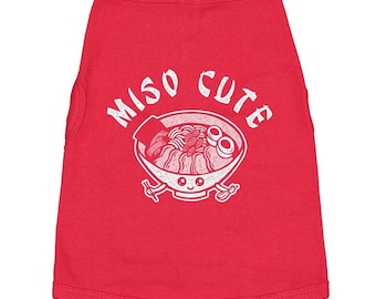 May include: A bright red pet tank top featuring a white graphic print of a bowl of ramen with a smiling face. The text MISO CUTE is arched above the bowl, which includes illustrations of noodles, toppings, and chopsticks on the sides.