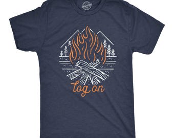 May include: A navy blue short-sleeve t-shirt featuring a graphic print of a campfire with orange flames and white logs. The design includes white outlines of mountains and pine trees in the background, with the orange text "log on" below.