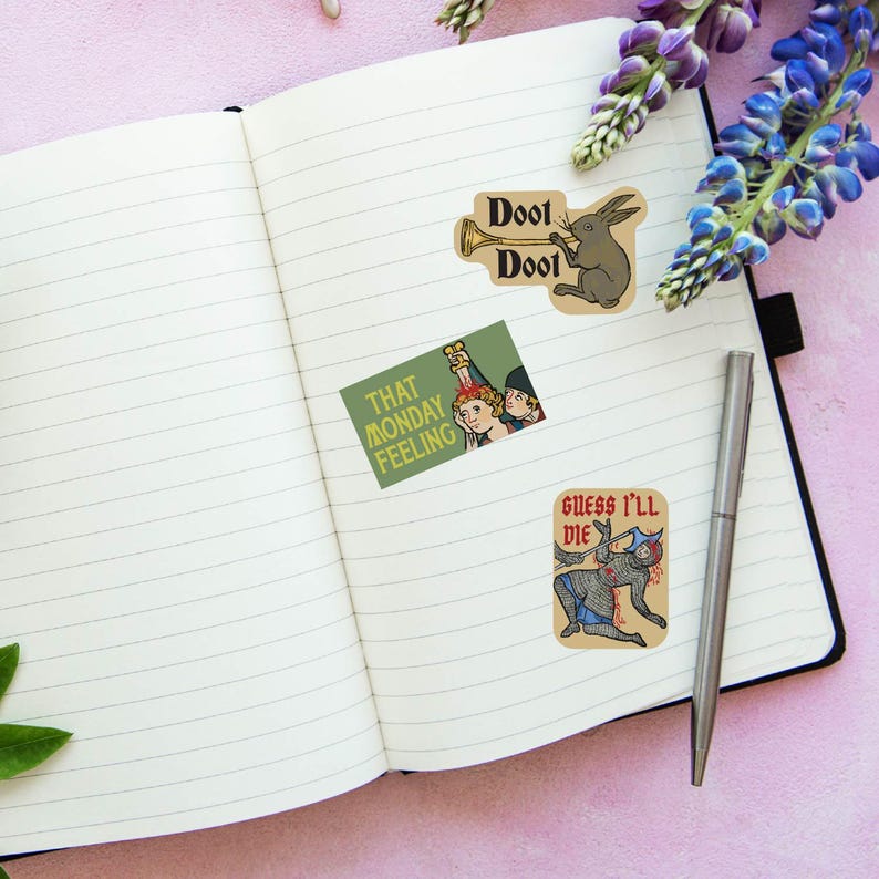 May include: An open notebook with lined pages, featuring three humorous stickers. One sticker shows a rabbit playing a trumpet with the text "Doot Doot." Another says "That Monday Feeling," and the last reads "Guess I'll Die."
