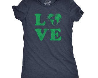May include: A dark navy blue short-sleeve t-shirt featuring the green text "LOVE" printed on the front. The letter "O" is replaced by a green heart shape containing a map of the world. The interior neck label displays the text "CRAZY DOG TSHIRTS.COM".