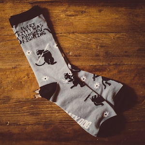 May include: A pair of gray socks with a black cat design and the text "Every kitty was kung fu fighting".