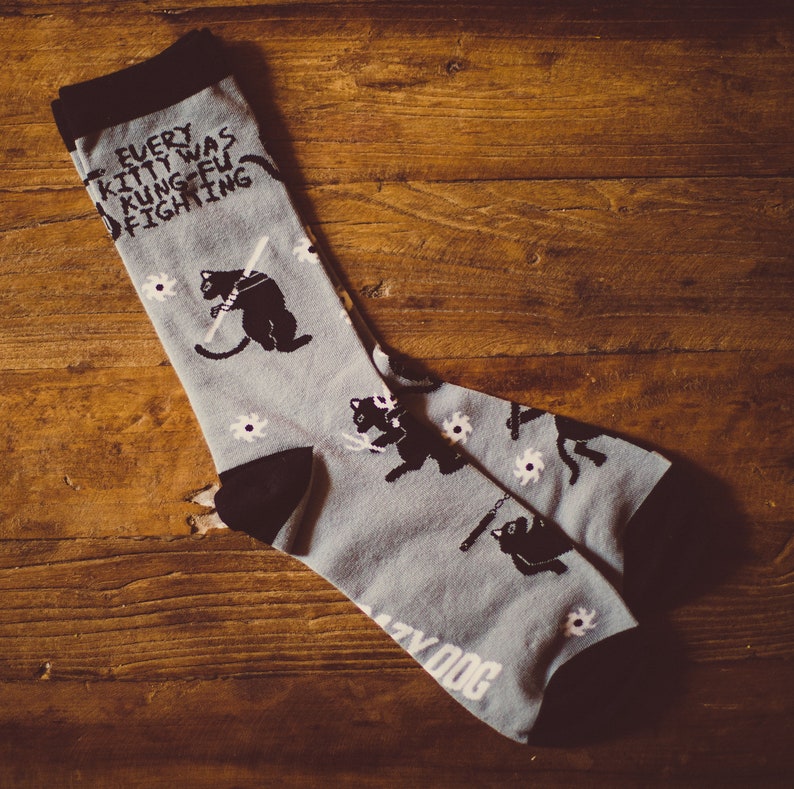 May include: A pair of gray socks with a black cat design and the text "Every kitty was kung fu fighting".
