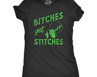 May include: A charcoal gray short-sleeve t-shirt featuring a bright green graphic of a female monster with a tall hairstyle. The text BITCHES get STITCHES is printed in green, with the letters styled to look like they are stitched together.
