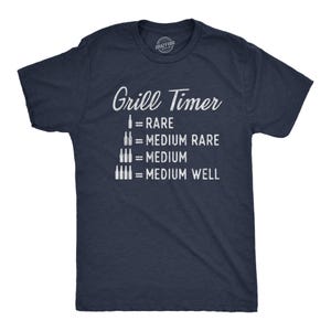 May include: A navy blue short-sleeve t-shirt featuring white text that reads Grill Timer followed by a graphic list of beer bottles equating to steak doneness levels: 1 bottle equals Rare, 2 bottles equal Medium Rare, 3 bottles equal Medium, 4 bottles equal Medium Well.