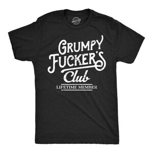 Könnte beinhalten: Ein schwarzes Kurzarm-T-Shirt mit weißem Text im Used-Look auf der Brust, der "GRUMPY FUCKER'S Club" lautet, sowie den darunter in kleinerer Schrift gedruckten Worten "LIFETIME MEMBER", alles mittig auf der Vorderseite des Kleidungsstücks.