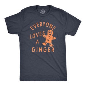 Puede incluir: Una camiseta azul marino con el texto "Everyone loves a ginger" en letras naranjas. También se incluye un gráfico de un hombre de jengibre en naranja.