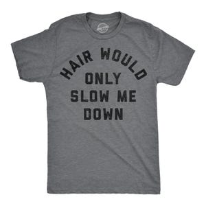 May include: A charcoal grey short-sleeve t-shirt with a crew neckline. The front features black, textured, block-letter text that reads: HAIR WOULD ONLY SLOW ME DOWN. The fabric has a heathered appearance with a visible weave and a small logo at the neck.