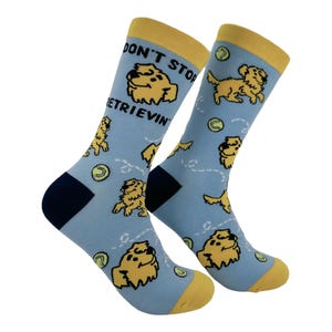 May include: A pair of light blue socks with a yellow cuff and toe. The socks feature a repeating pattern of yellow cartoon dogs and tennis balls, with the text "DON'T STOP RETRIEVIN'" on the cuff.