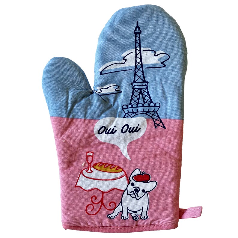 May include: Pink and blue oven mitt with a cartoon image of the Eiffel Tower, a dog, and a table with a baguette and a glass of wine. The text "Oui Oui" is in a speech bubble above the dog.