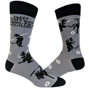 May include: A pair of gray socks with black and white illustrations of cats fighting with swords and throwing ninja stars. The socks have a black cuff and the text "EVERY KITTY WAS KUNG-FU FIGHTING" is printed on the front of the socks.