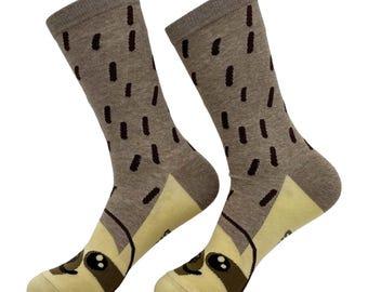 May include: A pair of crew socks featuring a light brown base with dark brown dash patterns. The toe and heel sections are a pale cream color, with a stylized sloth face graphic printed across the toe area, including dark brown eyes and a nose.