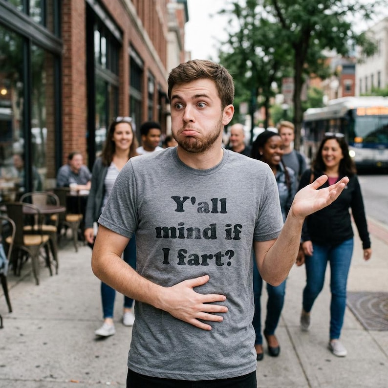 Puede incluir: Una camiseta gris jaspeado de manga corta con el texto negro Y'all mind if I fart? impreso en la parte delantera. La prenda tiene cuello redondo y un corte est&aacute;ndar, confeccionada en un tejido suave con una textura jaspeada visible.