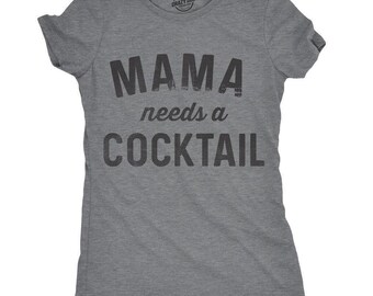 Puede incluir: Una camiseta gris jaspeado de manga corta con el texto negro MAMA needs a COCKTAIL impreso en la parte delantera. La prenda tiene un cuello redondo y un corte estándar, con el texto presentado en un estilo de fuente texturizado y desgastado.