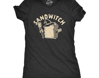 May include: A charcoal gray short-sleeve t-shirt featuring a graphic of a slice of bread wearing a witch hat and holding a broom. Above the character, the text SANDWITCH is printed in a cream-colored, distressed font. The shirt has a crew neckline.