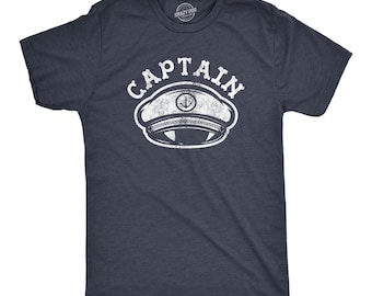 May include: A dark navy blue short-sleeve t-shirt featuring a white distressed graphic print on the chest. The graphic displays the word CAPTAIN in an arched font above a nautical captain's hat illustration with an anchor symbol in the center.