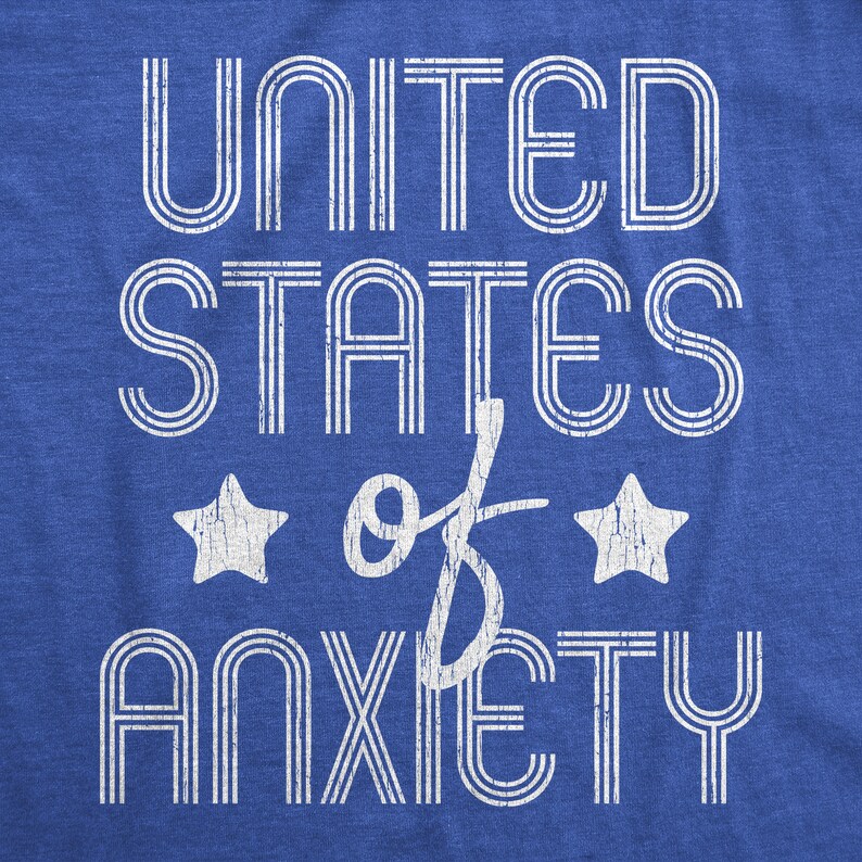 May include: Blue t-shirt with the text "UNITED STATES of ANXIETY" in white, distressed lettering. Two white stars flank the word "of". The shirt has a classic, vintage style.