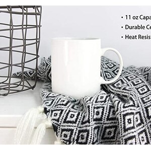 May include: White ceramic mug with a 11 ounce capacity. The mug is heat resistant and has a handle. The mug is sitting on a black and white patterned blanket.