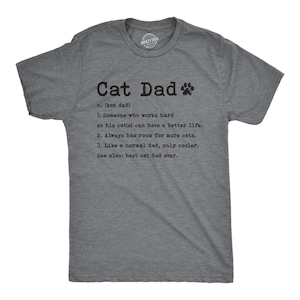 May include: A heather gray short-sleeve t-shirt featuring black text that reads Cat Dad, n. (kat dad), 1. Someone who works hard so his cat(s) can have a better life. 2. Always has room for more cats. 3. Like a normal dad, only cooler. See also: best cat dad ever.