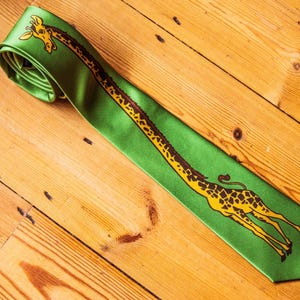 May include: A bright green necktie featuring a long, continuous illustration of a giraffe that stretches from the top rolled section down to the pointed tip. The giraffe is yellow with brown spots and a long neck extending along the fabric.