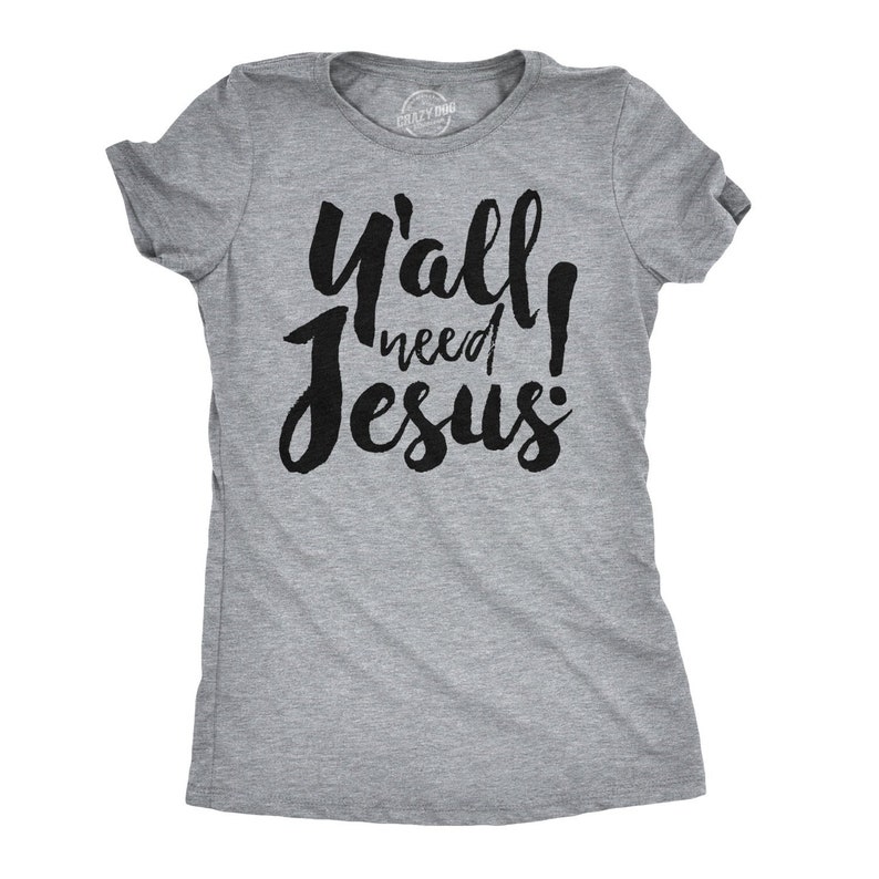 May include: A heather gray t-shirt with the text "Y'all need Jesus" in bold, black script. The shirt has short sleeves and a crew neck. The brand name "Crazy Dog" is printed on the neckline.