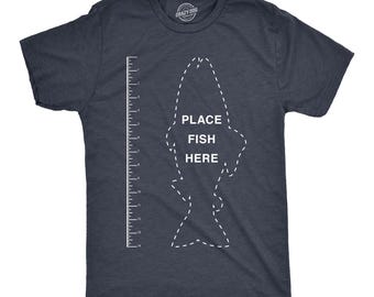 May include: A dark heather navy blue short-sleeve t-shirt featuring a white dashed outline of a fish, a vertical ruler marked in centimetres from 1 to 35, and the white text "PLACE FISH HERE" printed in the centre of the fish graphic.