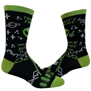 May include: Black crew socks with lime green cuffs, heels, and toes. The socks feature a space-themed pattern with white stars, planets, UFOs, green alien heads, pine trees, and mountains. Text on the socks reads "TONIGHT FORECAST" and "100% CHANCE OF STUFF".